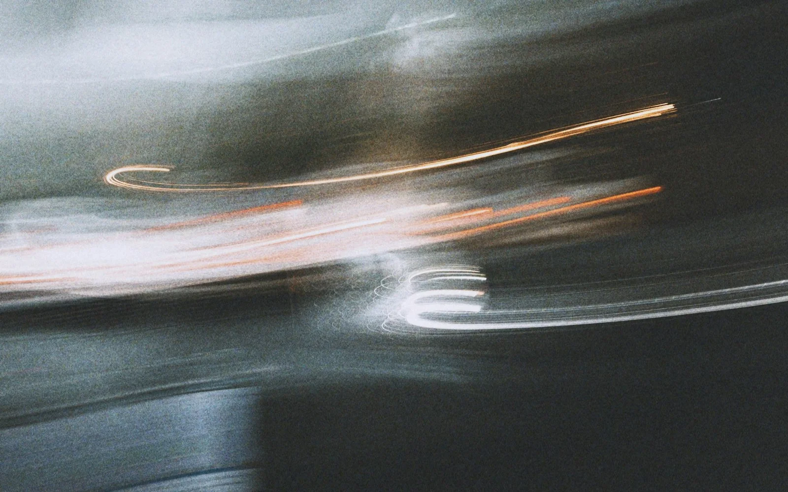 A motion-blurred night scene in grey and green, cut by one thin amber light trail.